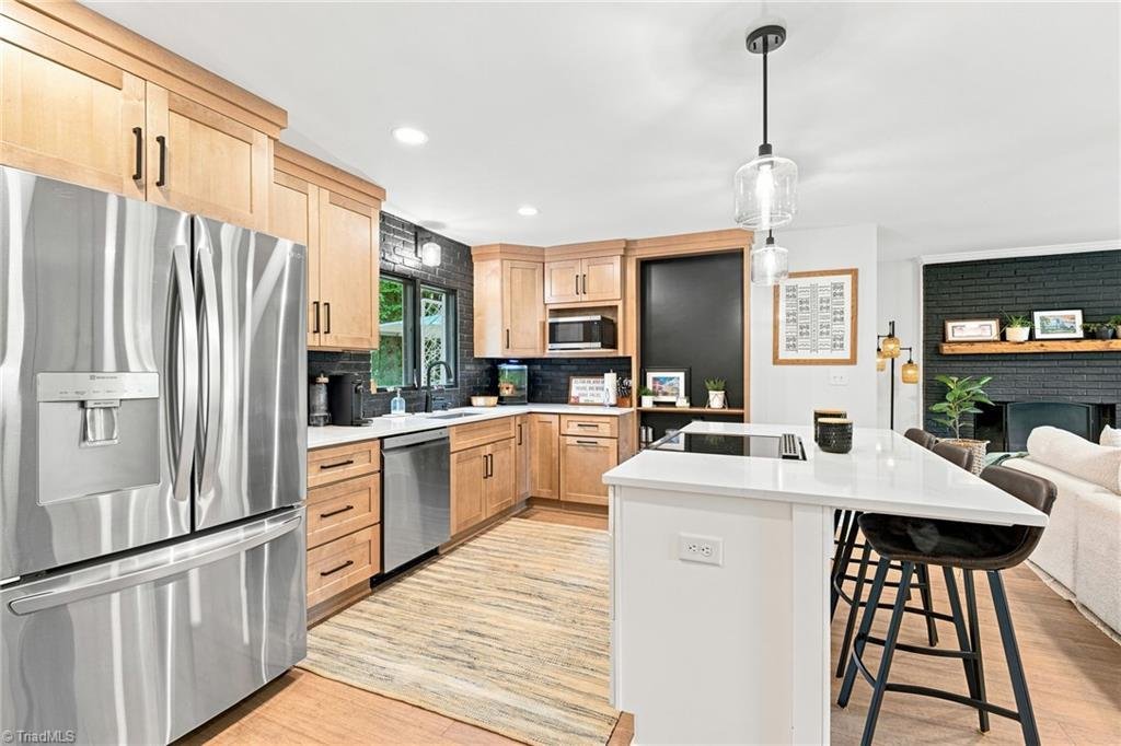 1450 Old Coach Road Kernersville NC renovated main kitchen — natural wood cabinetry, black brick backsplash, quartz island with stainless appliances and pendant lighting